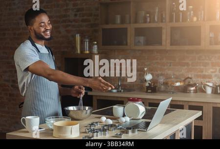 Black man baking pastry and using laptop in kitchen Stock Photo