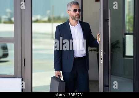 Business man entering an office building. Mature businessman walking into a meeting. Business man stepping through an office door. Charismatic Stock Photo