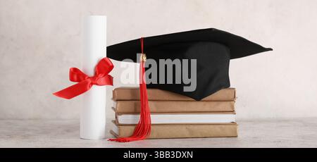 Mortar board, stack of books and diploma on light background Stock Photo
