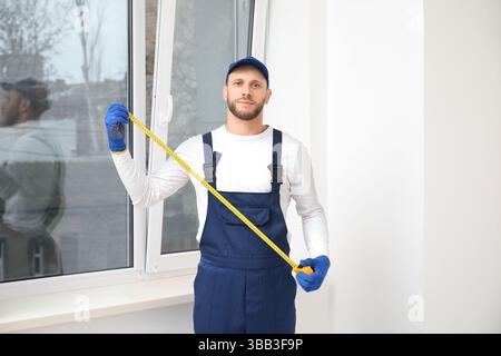 Male worker with tape measure near window in room Stock Photo