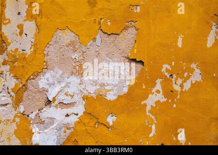 Weathered yellow wall with peeling paint and textured surface. Stock Photo
