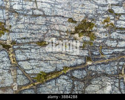 Uneven rock surface with noticeable moss patches and deep cracks. Stock Photo