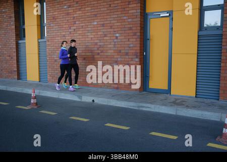 Two adults jogging together along an urban sidewalk on a sunny day Stock Photo