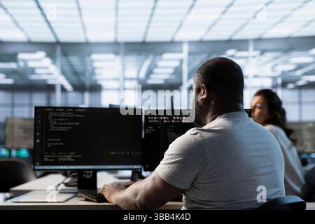 Technician in server farm workspace protecting data threatened by hacking attacks on computers. African american IT professional writing code, safeguarding data center from unauthorized access Stock Photo