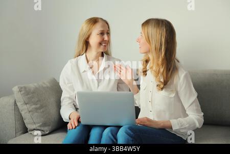 Happy smiling two business women talking while working on laptop using computer together, caucasian female colleagues in white shirts looking at each Stock Photo