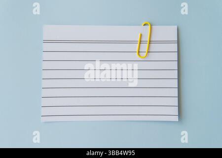 Minimal school paper concept with lined sheet and yellow paperclip on blue background symbolizing writing planning simplicity schoolwork education Stock Photo