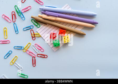 Creative school supplies flatlay with colorful paints markers paper clips clock yellow school bus brushes and punches arranged on light blue Stock Photo