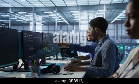 Cheerful coworkers in data center implementing AI predictive maintenance systems. Server room engineers using artificial intelligence to identify hardware failures impacting operations, camera A Stock Photo