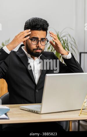 Unhappy Indian businessman programmer software developer working on laptop loses becoming surprised by bad news results, fortune loss fail at home office. Deadline, bankruptcy. Freelancer man Stock Photo