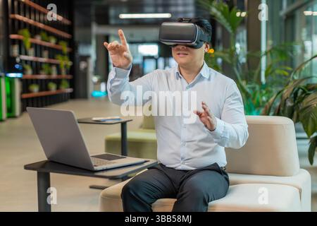 Middle-aged businessman programmer software developer using headset app making a presentation. Watching virtual reality 3D 360 video. Mature guy manager in shirt in VR goggles working at office lobby. Stock Photo