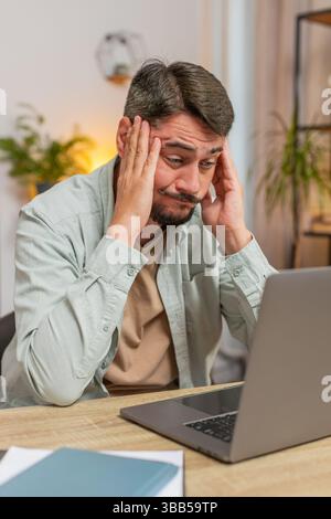 Angry furious man freelancer using laptop while working at home office having nervous breakdown at work, stress management, mental distress problems, losing temper, reaction on failure. Vertical. Stock Photo