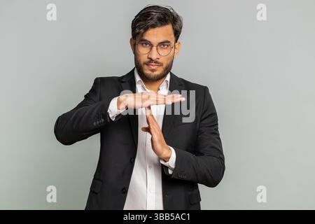 Tired serious upset Indian businessman showing time out gesture, limit or stop sign, no pressure, I need more time, take a break, relax, rest, help. Arabian man guy isolated on gray studio background Stock Photo
