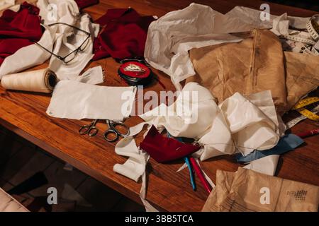 A busy workspace features fabric scraps, scissors, and sewing tools, highlighting the creative process in sewing. Stock Photo