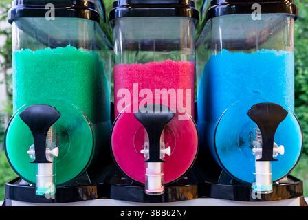 Three colorful frozen drink containers filled with slushy ice in green, pink, and blue, ready for dispensing on a hot day. Stock Photo