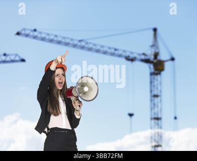 Young woman builder in hardhat screaming in megaphone Stock Photo