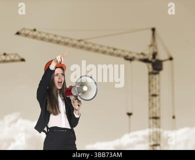 Young woman builder in hardhat screaming in megaphone Stock Photo