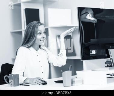 Young pretty business woman sitting at the desk with computer in blue office Stock Photo