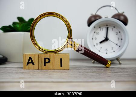 Magnifying glass and alarm clock with wooden blocks alphabet letters API text message on wooden background Stock Photo