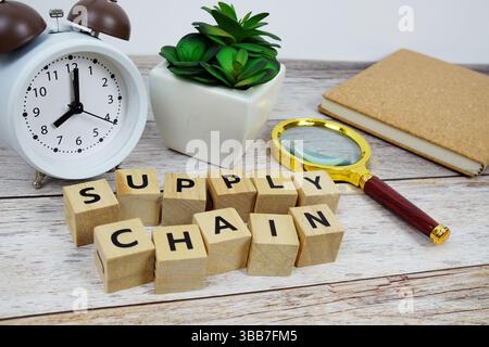 Magnifying glass and alarm clock with wooden blocks alphabet letters SUPPLY CHAIN text message on wooden background Stock Photo