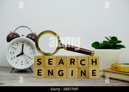 Magnifying glass and alarm clock with wooden blocks alphabet letters SEARCH ENGINE text message on yellow background Stock Photo