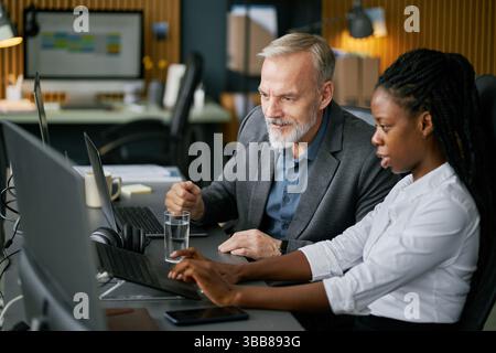 Businessman and businesswoman collaborating over laptop in office. Discussing strategies while working together with focus and engagement Stock Photo
