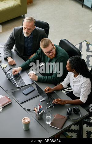 Group of business professionals discussing project strategy around conference table, with man pointing at laptop screen, engaging in productive discus Stock Photo