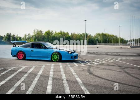 blue Nissan 200sx drifting in parking lot with smoke coming out of the rear arches. Side view of Nissan S14 powersliding on asphalt surface. Stock Photo