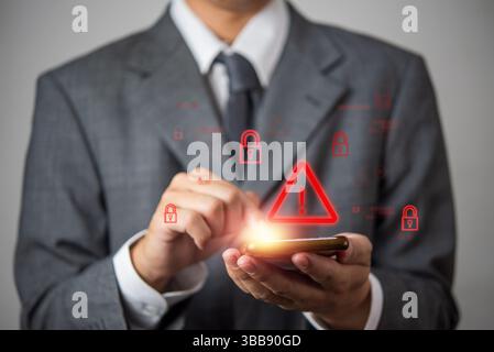 Cybersecurity warning concept with a businessman using a smartphone. Digital security threat, hacking risk, malware attack, and online data protection Stock Photo