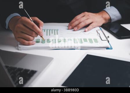 businessman analyzing financial reports and graphs with a pen at his desk, focusing on growth data. Stock Photo