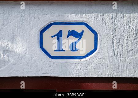Decorative Tile House Number Seventeen. Close-up of an ornate ceramic tile displaying the blue number '17' with a blue border, mounted on a textured l Stock Photo
