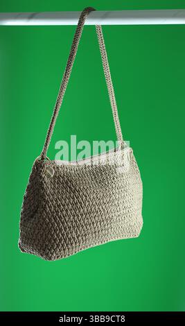 Beige crochet bag with marble pattern hanging on hanger. Isolated on green background. Stock Photo