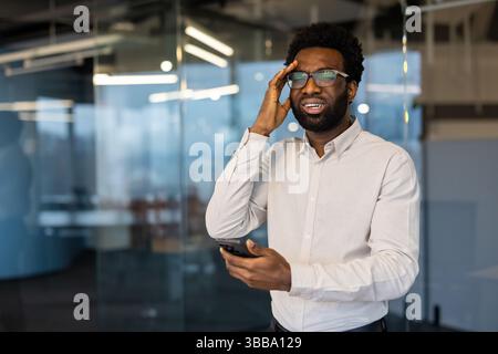 An african-american man reacts with dismay after reading a message on his mobile phone inside an office setting Stock Photo