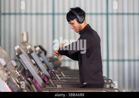 Workout and Fitness. Smiling man checking smartwatch while using treadmill in a gym. Stock Photo