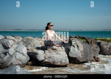 sporty woman sitting on rocks by the sea meditating Stock Photo
