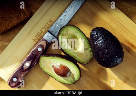 Three avocados and knife lie on the wooden cutting board. View from the top Stock Photo