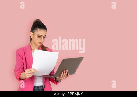 busy business woman manager, lawyer, accountant holding documents and laptop. Checking financial reports, working. Isolated pastel pink background Stock Photo