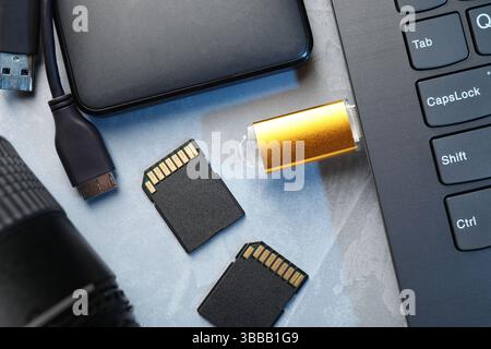 Flash drive connected to laptop, SD memory cards, external hard disk and camera lens on gray textured table, flat lay Stock Photo