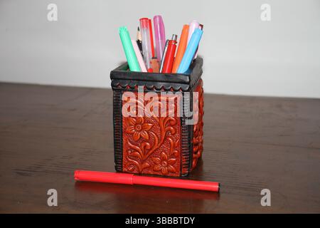 A red colored pen holder is holding various pens on a wooden surface. Stock Photo