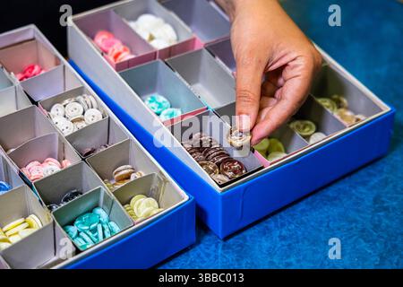 Hand picking a brown marbled button from a divided storage box filled with assorted buttons in a craft or fabric store, showcasing variety Stock Photo