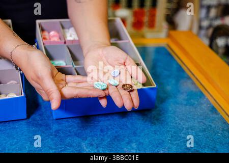 Close-up of hands comparing pastel blue and brown buttons from a button box in fabric store, focusing on detail and variety in sewing accessories Stock Photo