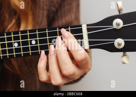 Woman playing ukulele chords. Female fingers on strings. Learning guitar music. Soft natural lighting. Musical instrument detail. Stock Photo