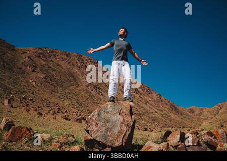 Handsome successful man standing with closed eyes on a huge boulder in mountains Stock Photo