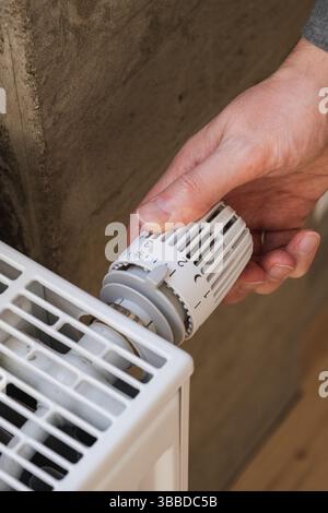 Man's hand adjusting temperature on heating radiator Stock Photo