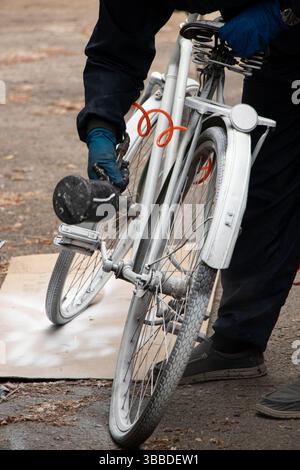 Painting an old bicycle with an airbrush outdoors in white, bicycle restoration, paint Stock Photo