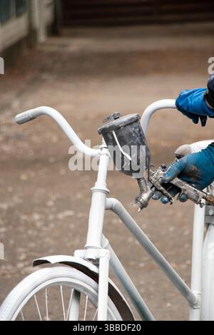 Painting an old bicycle with an airbrush outdoors in white, bicycle restoration, paint Stock Photo