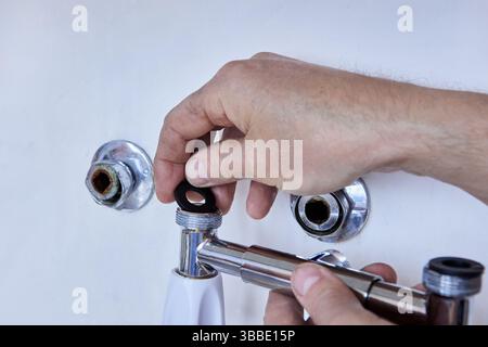 Hands prepare installation of wall mounted dual handle faucet by placing sealing washer on fitting, shiny chrome escutcheons and open pipes visible. Stock Photo