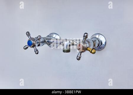 Old dual handle tap fixture with blue and red indicators, spout is missing after removal, visible wear and open outlet where water should flow. Stock Photo