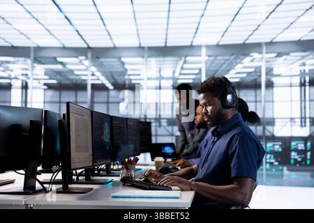 Man in data center workplace hearing songs in headset while using programming languages to build applications. Server hub software developer listening music, debugging code Stock Photo