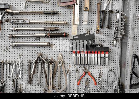 Assorted hand tools and socket wrenches neatly arranged on pegboard in workshop creating organized workspace for mechanical repairs and maintenance tasks Stock Photo