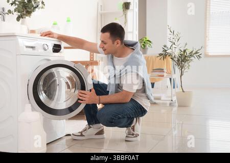 Young man using washing machine in laundry room Stock Photo
